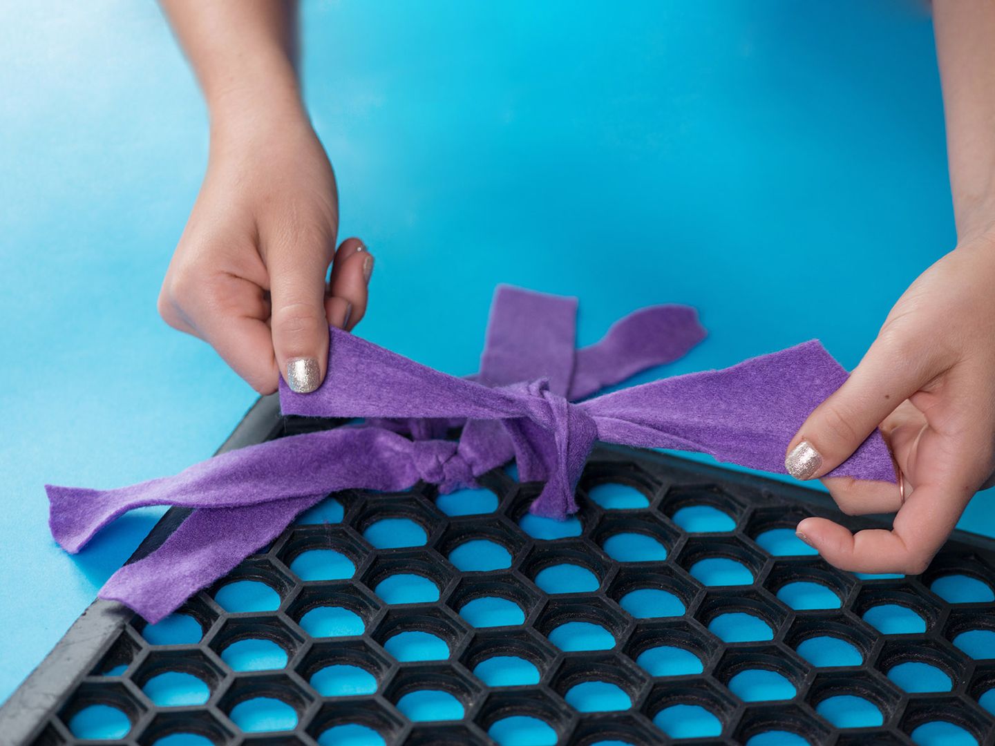 Close up of someone's hands tying felt into holes in a rubber mat