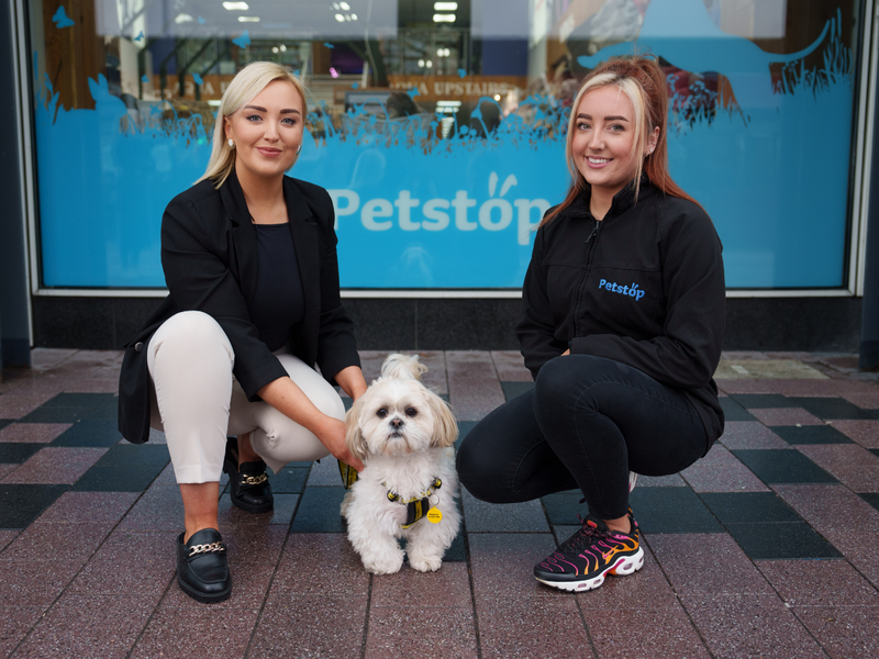 Two women kneeling with a dog in the middle outside a PetShop store